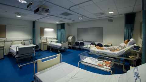 A room with four hospital beds and a baby's cot.