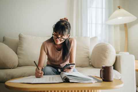 woman writing on paper while sitting on sofa