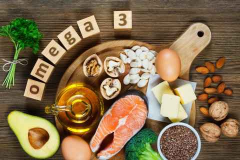Salmon, avocado, broccoli, nuts, seeds and an egg with 'omega 3' written on wooden blocks.