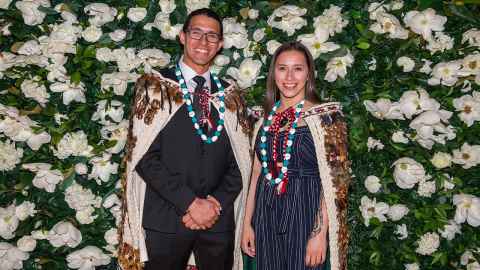 Two smiling people, wearing traditional korowai.