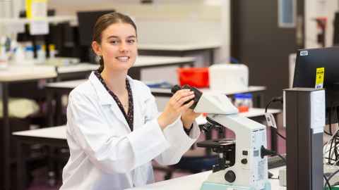 A young woman in a lab coat, at a microscope.