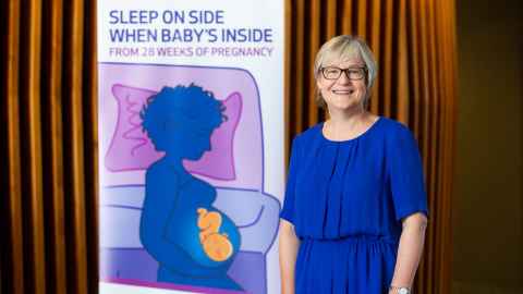 A woman in a blue dress standing next to a poster that says 'Sleep on side when baby's inside'.