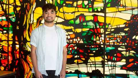 A young man standing in front of a stained glass window.