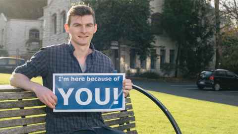 Scholarship student holding a sign saying "I'm here because of you!"
