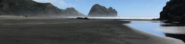 South Piha, clear blue sky and black sands with Camel Rock in the background