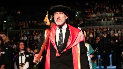 Photo of Peter Shand carrying the ceremonial mace. He is dressed in his doctoral regalia. 