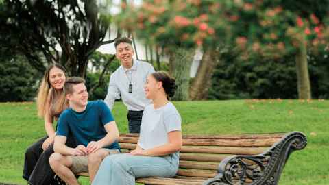 Photo of four students sitting on a bench in Albert Park. The students are talking to one another. 