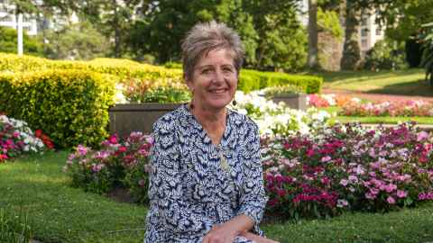 Photo of Nikki Mandow sitting in front of a floral garden. 