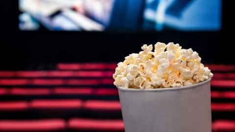 Photo of a bucket of popcorn with cinema seats and screen in the background.