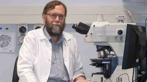 Photo of Professor Alistair Gunn in his lab coat. He is sitting in a lab. 