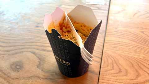 Photo of an open takeaway food box containing a tomato-based pasta. There is also a fork perched on top of the box diagonally. 