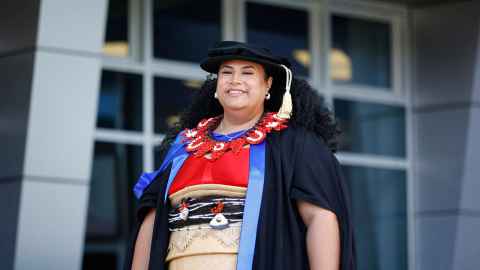 Dr Penni Wolfgramm outside Spark Arena in doctoral regalia (black velvet bonnet with gold cord, black robe with blue satin edging) and traditional Tongan dress
