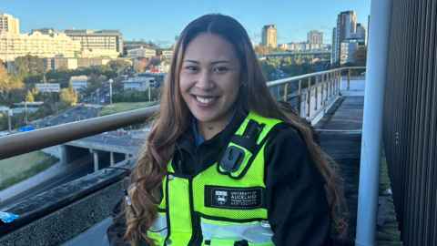 Amelia smiling at the camera wearing a security vest with the city in the background