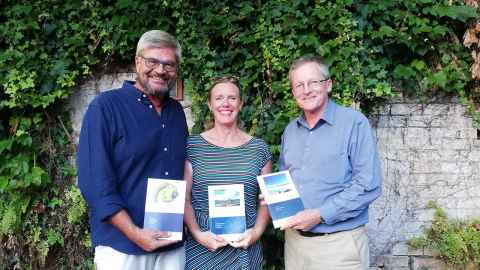 Two men and a woman holding books.