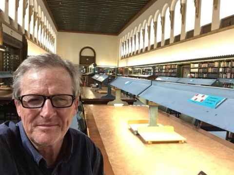 A library with desks at the centre of the room and shelves of books on the walls.