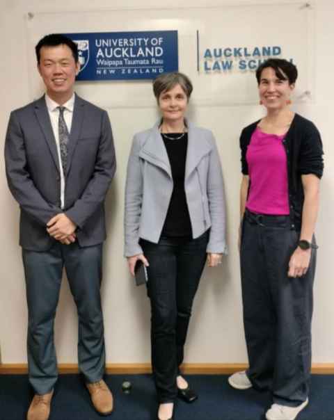Three people in front of a sign with the Auckland Law School logo.