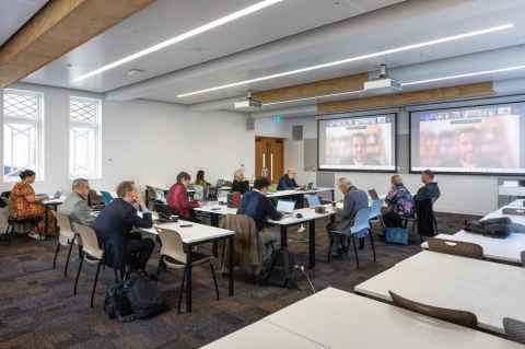 A classroom filled with people watching screens at the front of the room.