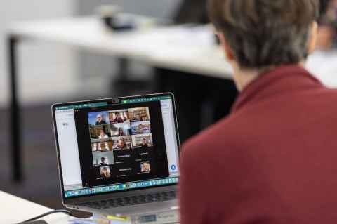A person watching an online meeting on a laptop.