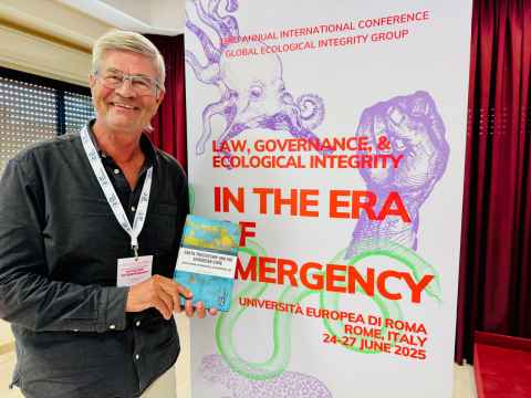 A man holding a book, standing in front of a sign.