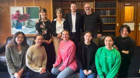 A group of people with bookshelves, a painting and wood panelling in the background.