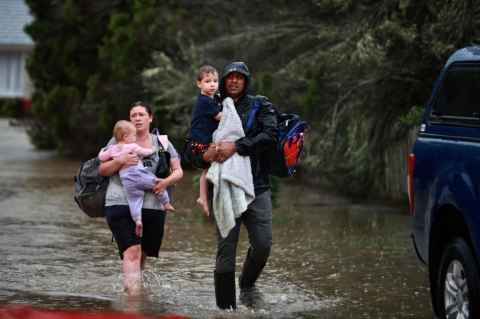 A man and woman walking through floodwaters carrying small children.