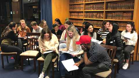 Students seated in a room full of bookshelves, working together with pen and paper.