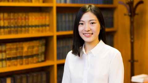 Photograph of Jessie Jiang standing in front of shelves of Law books.