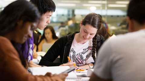 Four students sitting at a desk with notebooks, attending an exam preparation workshop.