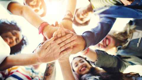 Low-angle view of a group of smiling students in a team huddle, stacking their hands together in unity.