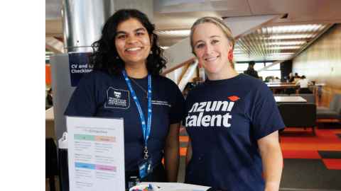 Two friendly career support staff standing behind a table smiling. 