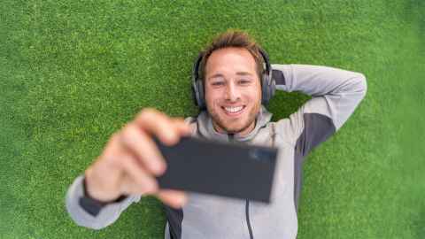 Male student laying on grass using their phone.