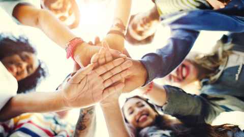 Photo of students joining their hands in the middle of a circle. 