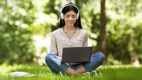 Photo of a student sitting outside on the grass with their laptop.