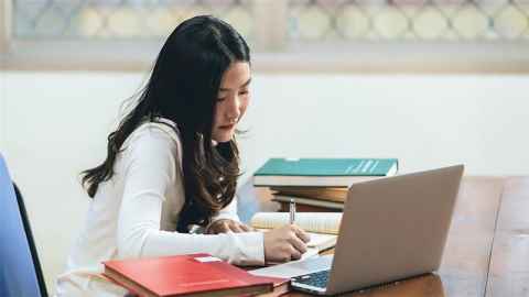 Photo of a student studying in front of her laptop on a desk covered in books from the Library