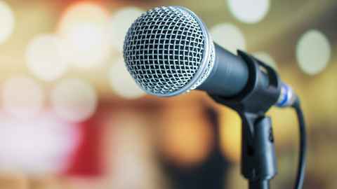 A photograph of a microphone on a stand with a blurred colourful background. 