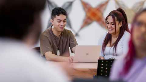 Woman reading book next to man at laptop. Both smiling.