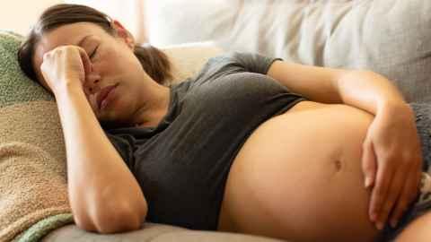 Pregnant woman lying on sofa holding belly