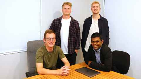 Four team members, two sitting at a table and two standing behind them