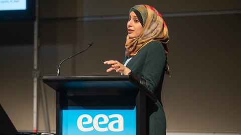 Safa Al-Sachit speaking from a podium that has an EEA logo