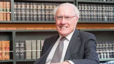 Sir Geoffrey Palmer sitting in front of shelves of law books