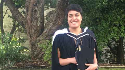 Fa'amu Ioane wearing academic regalia and standing in front of gardens outside the ClockTower