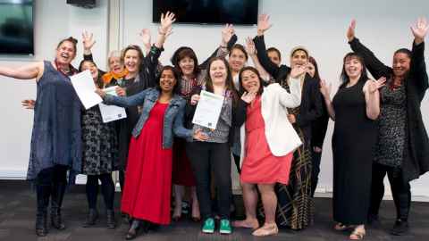A group of students holding certificates and waving their arms in celebration