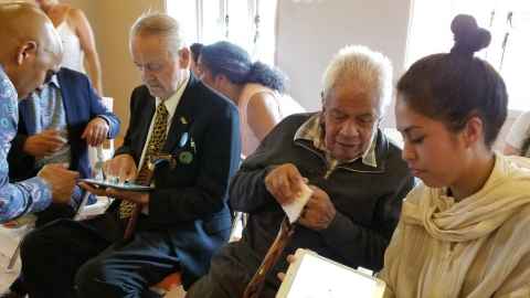 A group of people, including Joe and Bob Hawke, looking at tablet screens.