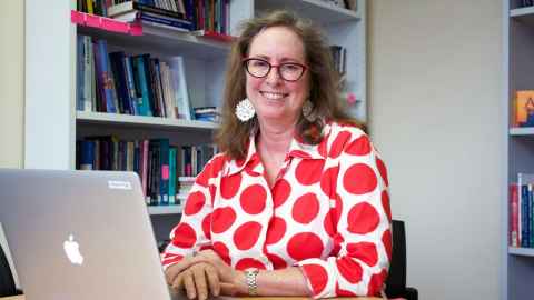 Professor Missy Morton sitting at a desk with a laptop, with bookshelves behind her.