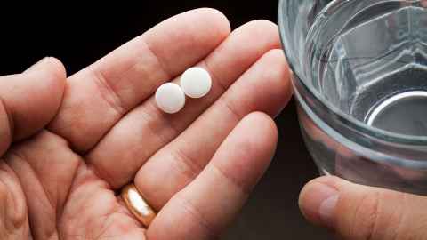 A person holding two asprin in one hand and a glass of water in the other
