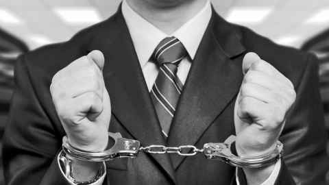 Black-and-white picture of a man wearing a suit, in handcuffs.