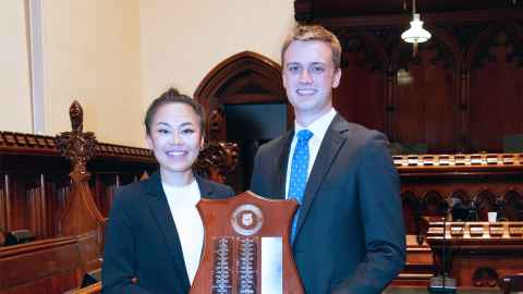 Diana Qiu and Michael Greatrex in a courtroom holding the Stout Shield