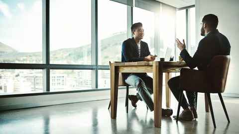 Two people having a conversation, seated at a table in an office
