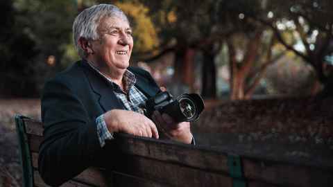 Gottfried Boehnke sitting on a park bench holding a camera