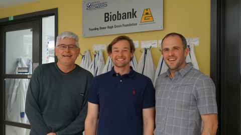 Professor Mike Dragunow, Taylor Stevenson and Dr Victor Dieriks standing under a sign with the logo and name of the Centre for Brain Research biobank.